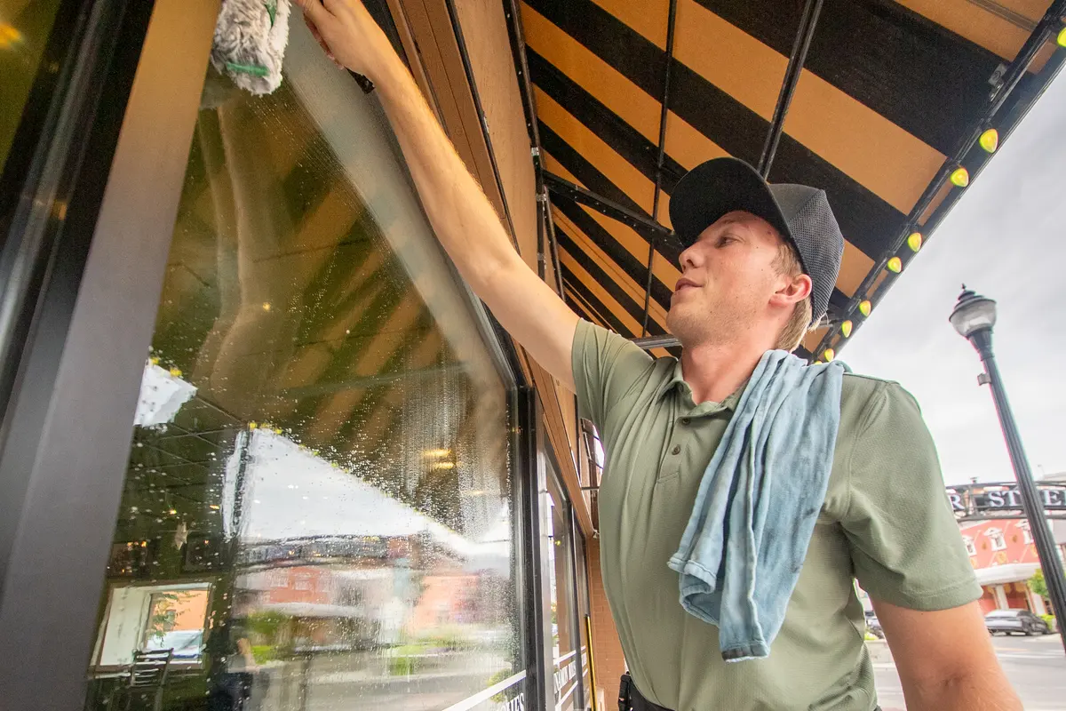 Lucas reaching a high storefront pane under the Great Harvest awning